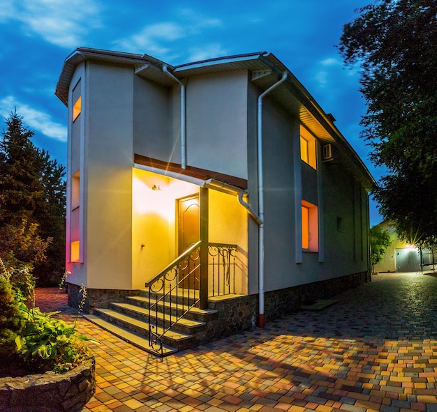 Vue horizontale de la maison unifamiliale avec patio. Manoir. Soirée. Lumière jaune des fenêtres