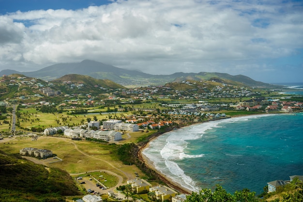 Une vue sur l'île de Saint-Kitts avec quartier résidentiel et plage au premier plan et collines verdoyantes