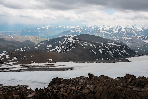 Vue imprenable depuis la colline de pierre avec des pierres pointues jusqu'aux montagnes enneigées sous un ciel nuageux Paysage alpin à très haute altitude avec nébulosité Paysage atmosphérique avec chaîne de montagnes enneigées dans un ciel couvert