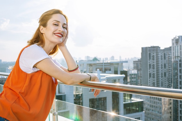 Vue imprenable. Joyeuse femme positive debout sur le balcon tout en profitant de la belle vue