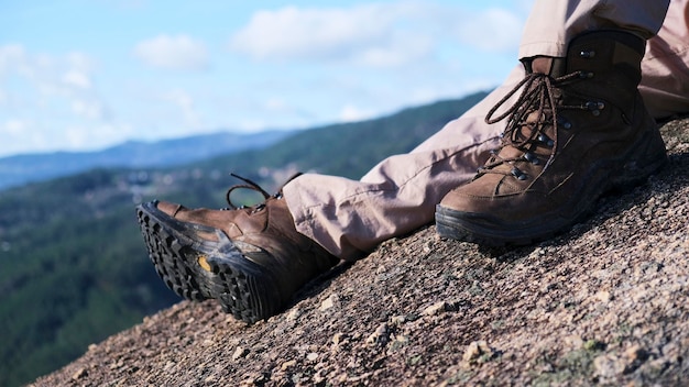 Photo vue des jambes et des bottes de l'homme sur un rocher au sommet de la montagne surplombant une vallée