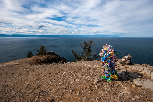 Vue sur le lac Baïkal depuis une falaise avec un tas de rubans sur une falaise sur un lieu sacré de l'île d'Olkhon. Nuages dans le ciel. Derrière le lac de montagne. Temps ensoleillé.