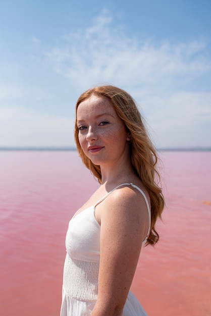 Vue latérale de l'adolescent mignon femme portant des vêtements d'été debout sur un magnifique lac rose