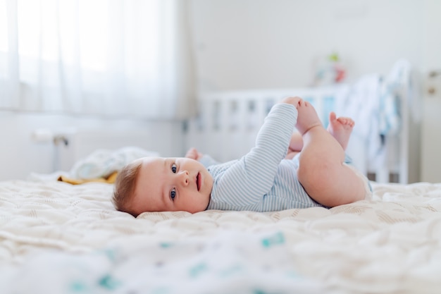 Vue latérale de l'adorable petit garçon de 6 mois caucasien habillé en body tenant ses pieds