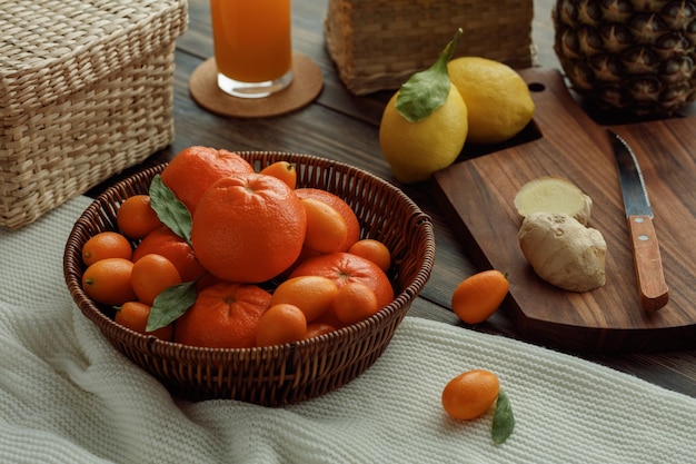 Vue latérale des agrumes comme le kumquat de mandarine dans le panier sur le tissu avec le jus d'orange de citron d'ananas sur le fond en bois