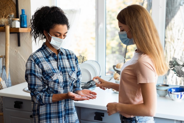 Vue latérale des amies avec des masques médicaux à l'aide d'un désinfectant pour les mains