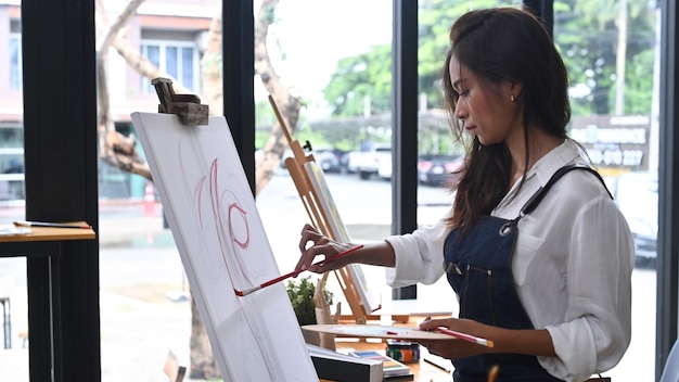 Vue latérale artiste féminine peignant à l'aquarelle sur chevalet dans un studio d'art