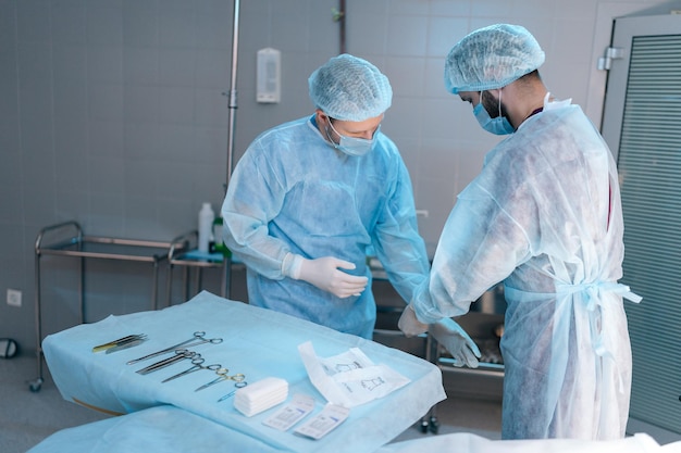 Vue latérale de l'assistant chirurgien masculin aidant à mettre des gants en latex avant l'équipe d'opération de
