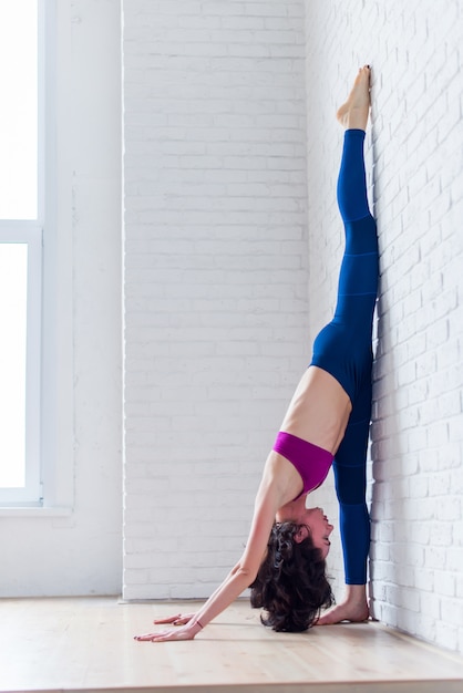 Vue latérale de l'athlète féminine professionnelle pratiquant le yoga qui s'étend de ses mollets, ischio-jambiers, cuisses faisant de l'exercice fractionné debout