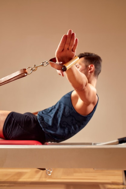 Vue latérale d'un athlète masculin pieds nus allongé sur un réformateur de pilates et effectuant des exercices d'abdominaux pendant l'entraînement physique Pilates man concept