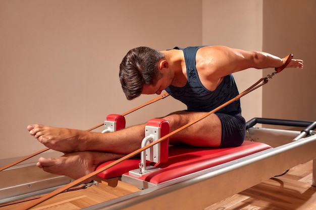 Vue latérale d'un athlète à pieds nus allongé sur un réformateur de pilates et effectuant un exercice abdominal pendant