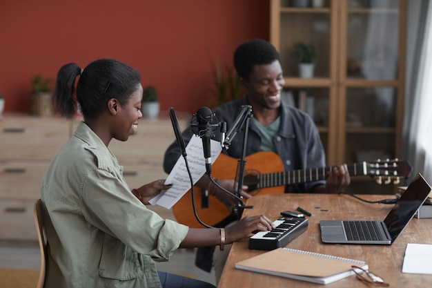 Vue latérale au jeune couple afro-américain composer de la musique ensemble en studio d'enregistrement à domicile