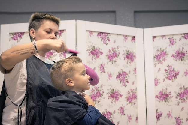 Photo vue latérale d'un barbier qui coupe les cheveux d'un garçon dans un salon