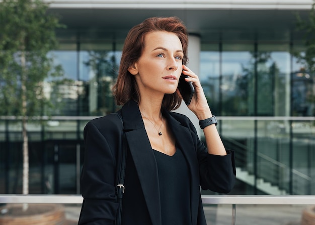 Vue latérale d'une belle femme d'affaires parlant sur un téléphone portable contre un bâtiment en verre