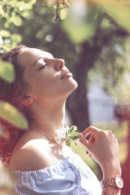 Photo vue latérale d'une belle femme aux yeux fermés tenant une fleur dans le parc