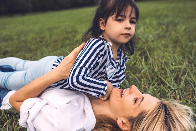 Vue latérale d'une belle femme jouant avec sa jolie petite fille sur l'herbe verte en plein air Aimer une jolie mère et sa fille heureuses passent du temps ensemble dans le parc Maman et enfant s'amusent Maternité heureuse