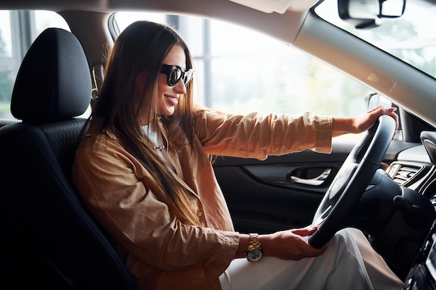 Vue latérale d'une belle jeune femme à la mode qui se trouve à l'intérieur de son automobile moderne