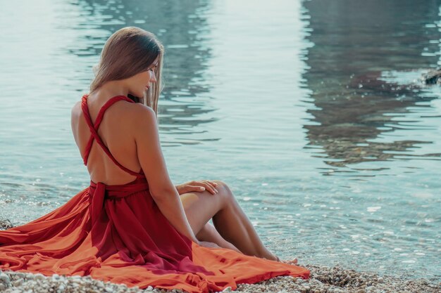 Vue latérale d'une belle jeune femme sensuelle vêtue d'une longue robe rouge posant près de la mer pendant