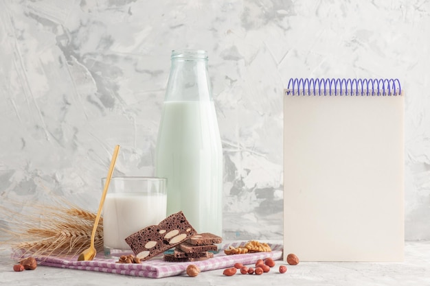 Vue latérale d'un bonbon en forme de bâton dans une bouteille en verre remplie de lait et de biscuits pointes de cacahuètes sur un cahier à spirale de serviette à rayures violettes sur fond blanc