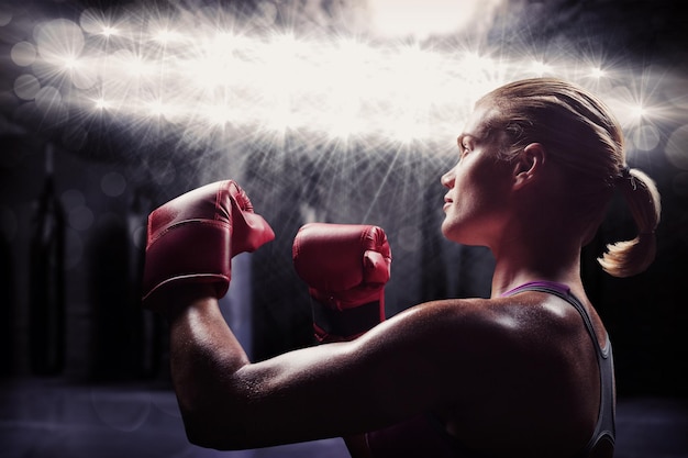 Vue latérale d'une boxeuse avec une position de combat contre une zone de boxe rouge avec des sacs de boxe