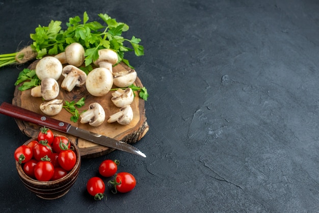 Vue latérale des champignons crus et couteaux verts sur planche de bois serviette blanche et tomates fraîches dans un bol sur fond noir avec espace libre