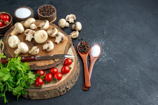 Vue latérale des champignons crus frais et des épices vertes de tomates de couteau de paquet sur une serviette en bois sur fond noir