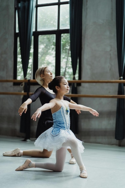 Vue latérale complète du corps d'une fille asiatique répétant des mouvements de ballet avec un instructeur personnel au cours de danse Sto