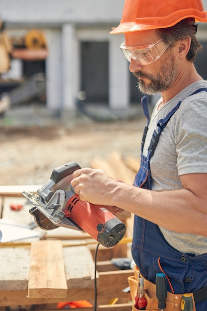 Vue latérale d'un constructeur masculin concentré dans des lunettes de sécurité regardant une scie circulaire