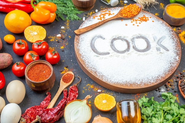 Vue latérale d'un cuisinier écrivant avec de la farine sur une planche de bois parmi des légumes frais, des épices, des paquets verts, une bouteille d'huile tombée sur un mur noir