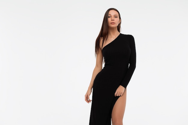 Vue latérale d'une dame sensuelle en robe noire sexy regardant la caméra sur fond blanc