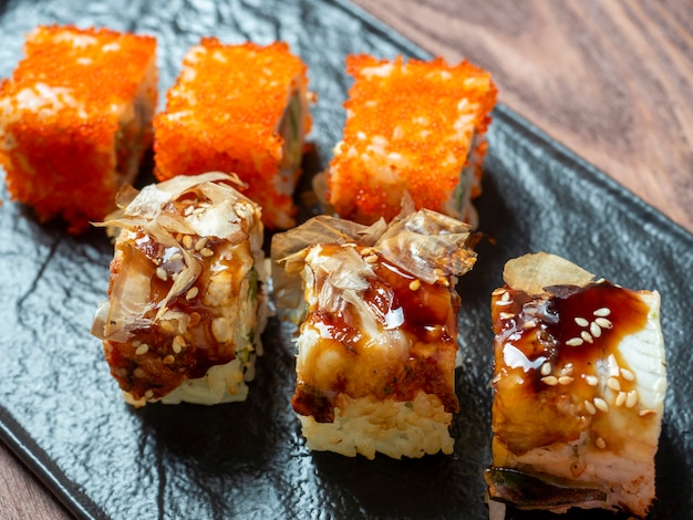 Vue latérale de délicieux petits pains juteux décorés de caviar. Cuisine japonaise, plaque noire, gros plan