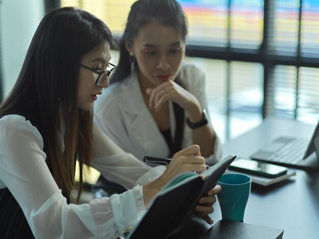 Vue latérale de deux jeunes femmes d'affaires consultant sur leur projet dans la salle de réunion