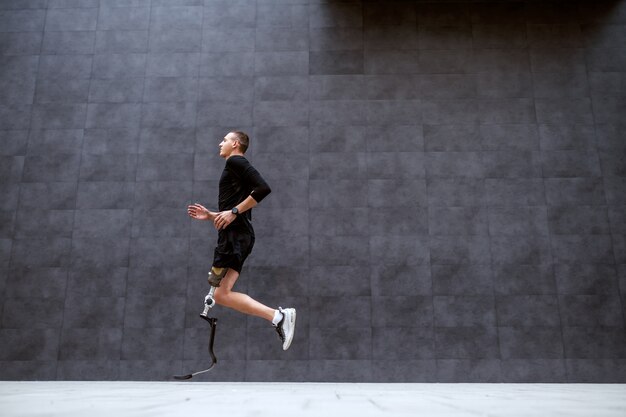 Photo vue latérale du beau sportif caucasien fit avec une jambe artificielle qui court à l'extérieur.