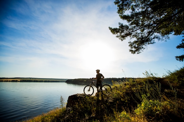 Vue latérale du cavalier sur un vélo debout sur un rocher et profiter du coucher du soleil. Motivation et inspiration pour l'aventure.