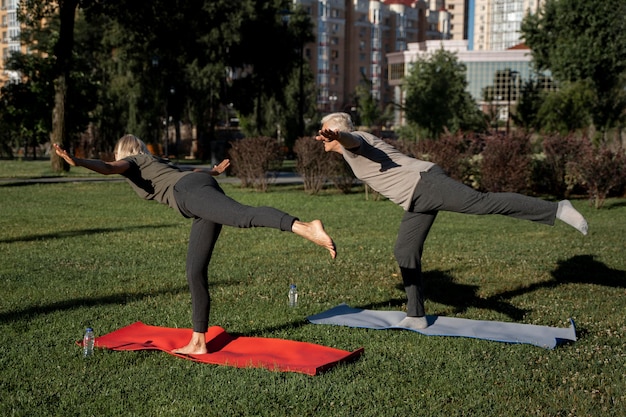 Vue latérale du couple de personnes âgées pratiquant le yoga à l'extérieur
