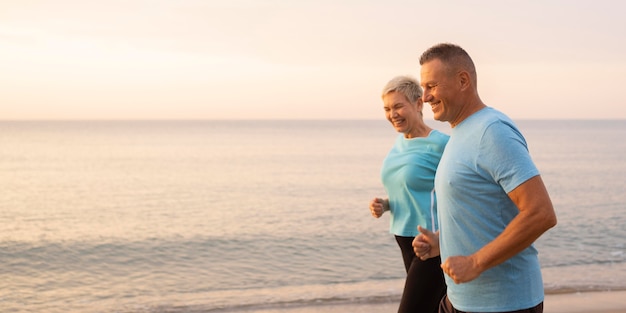 Vue latérale du couple senior jogging sur la plage ensemble