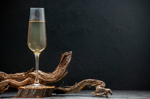 Vue latérale du gobelet avec du vin sur une planche à découper en bois et une branche d'arbre sur le côté droit sur la lumière sur fond sombre