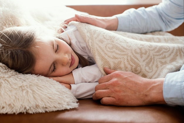 Vue latérale du père couvrant sa fille endormie avec une couverture