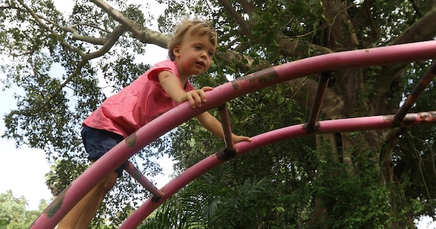 Vue latérale du petit garçon curieux grimper sur une échelle en métal sur l&#39;aire de jeux dans un parc verdoyant