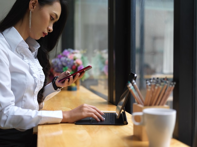 Vue latérale du pigiste féminin à l'aide de smartphone tout en travaillant avec une tablette numérique sur bar in cafe