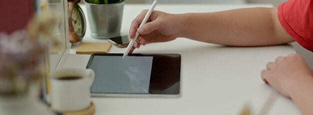 Vue latérale du pigiste travaillant sur une tablette numérique avec un stylet sur une table de travail blanche