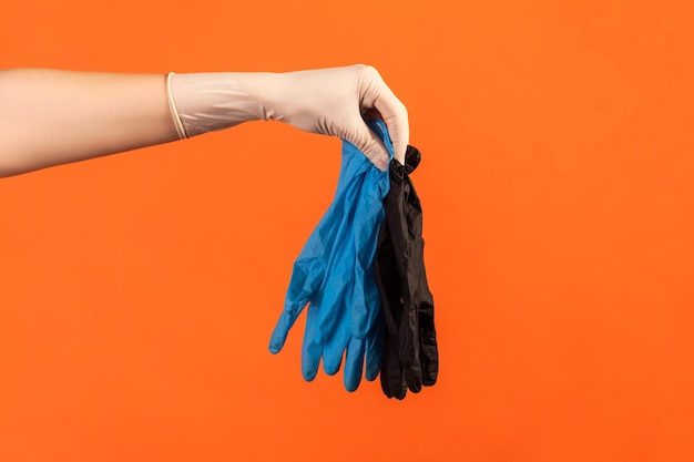 Vue latérale du profil en gros plan de la main humaine dans des gants chirurgicaux blancs tenant des gants bleus et noirs.