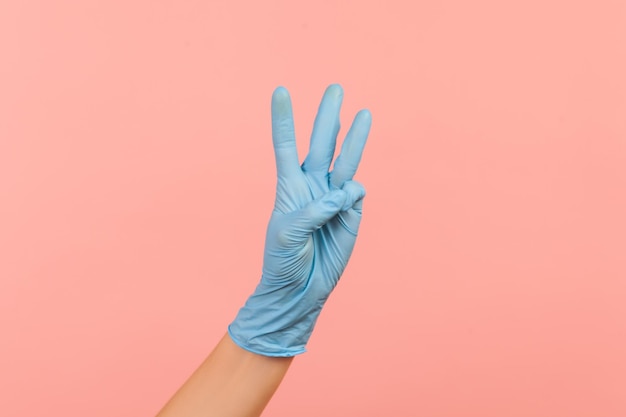 Vue latérale du profil gros plan de la main humaine dans des gants chirurgicaux bleus montrant le numéro 3 trois avec les mains