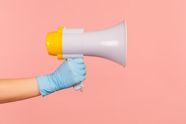 Vue latérale du profil gros plan de la main humaine dans des gants chirurgicaux bleus tenant un mégaphone.