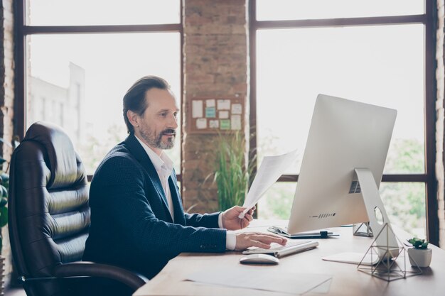 Vue latérale du profil portrait de son bel homme gai et concentré occupé, expert de l'employeur, dactylographie du plan de financement, rapport d'assurance à la station de travail de l'espace ouvert industriel industriel en brique loft moderne