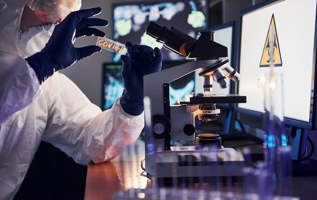 Vue latérale du scientifique en uniforme de protection blanc qui fonctionne avec le coronavirus en laboratoire