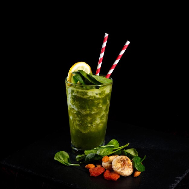 Vue latérale du smoothie vert avec des feuilles d'épinards frais sur le bureau du bar