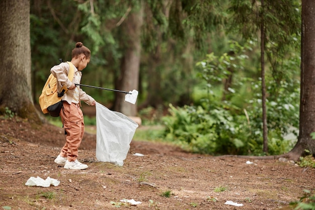 Vue latérale éco activiste petite fille ramassant le sentier des bouteilles en plastique