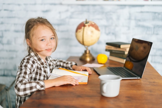 Vue latérale d'une écolière mignonne et gaie d'enfants faisant des devoirs d'écriture assis à table avec