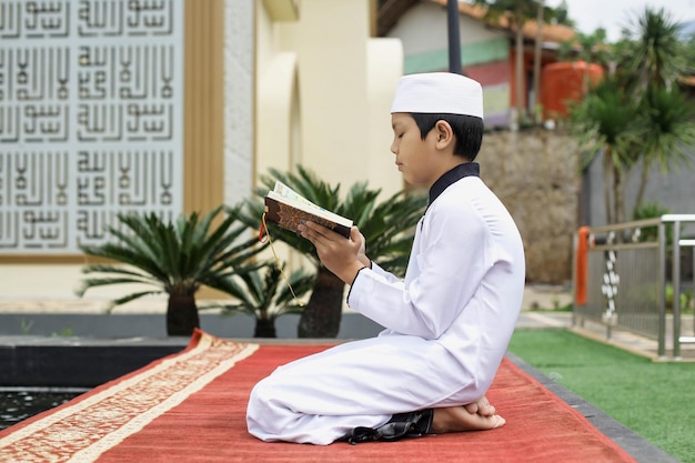Vue latérale Un élève d'un internat islamique lisant le Coran dans la cour de la mosquée